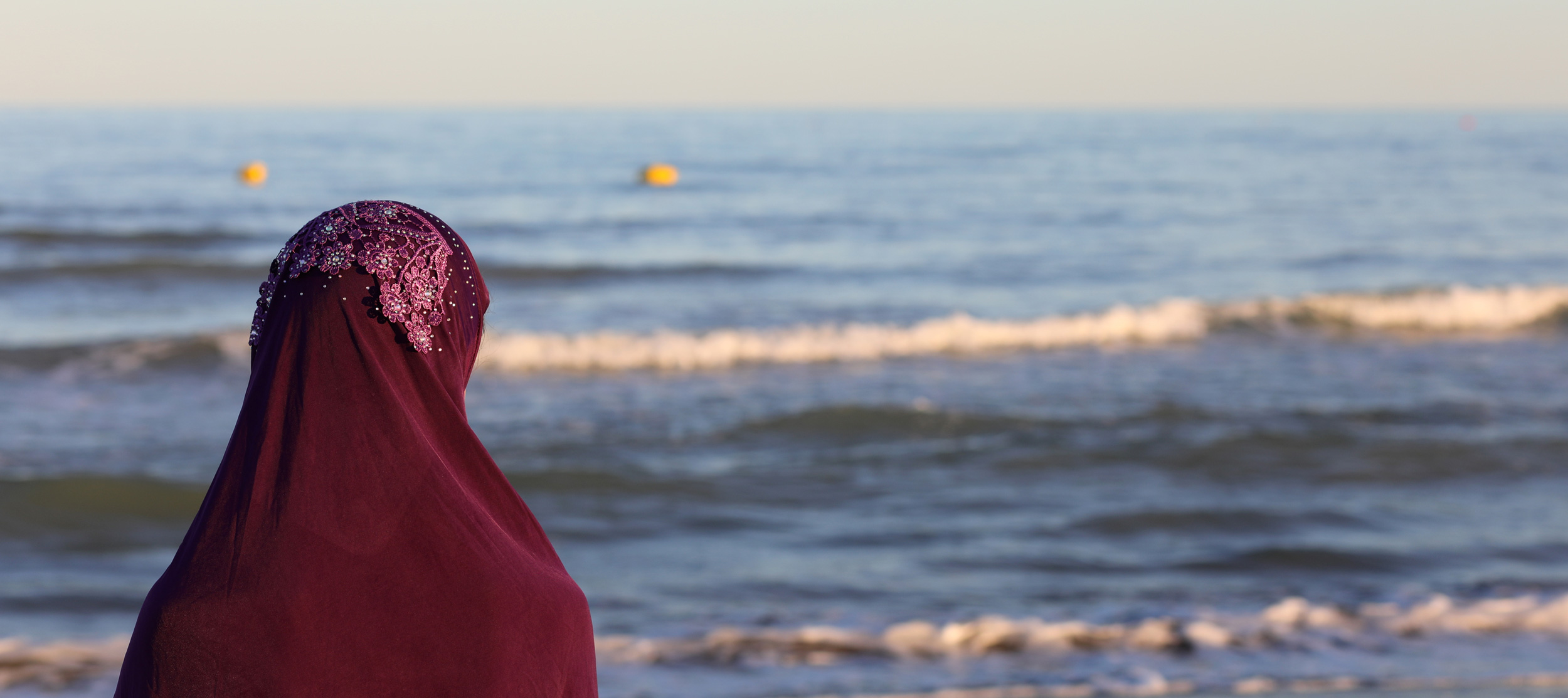 Woman with a veil on her head by the sea looking at the distance